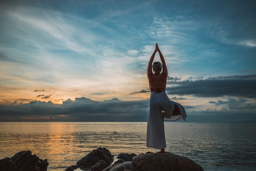 Mulher fazendo yoga de frente para o mar com o sol se pondo