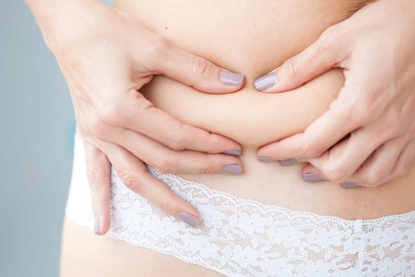Uma mulher apertando uma gordura localizada no flanco direito da sua cintura.