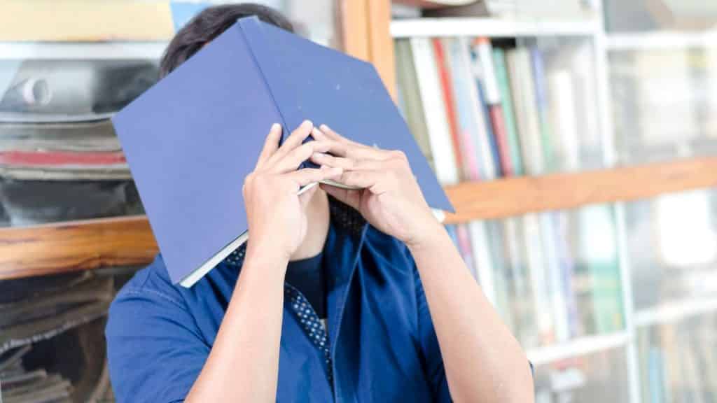 Um homem tapando seu rosto com um livro aberto.