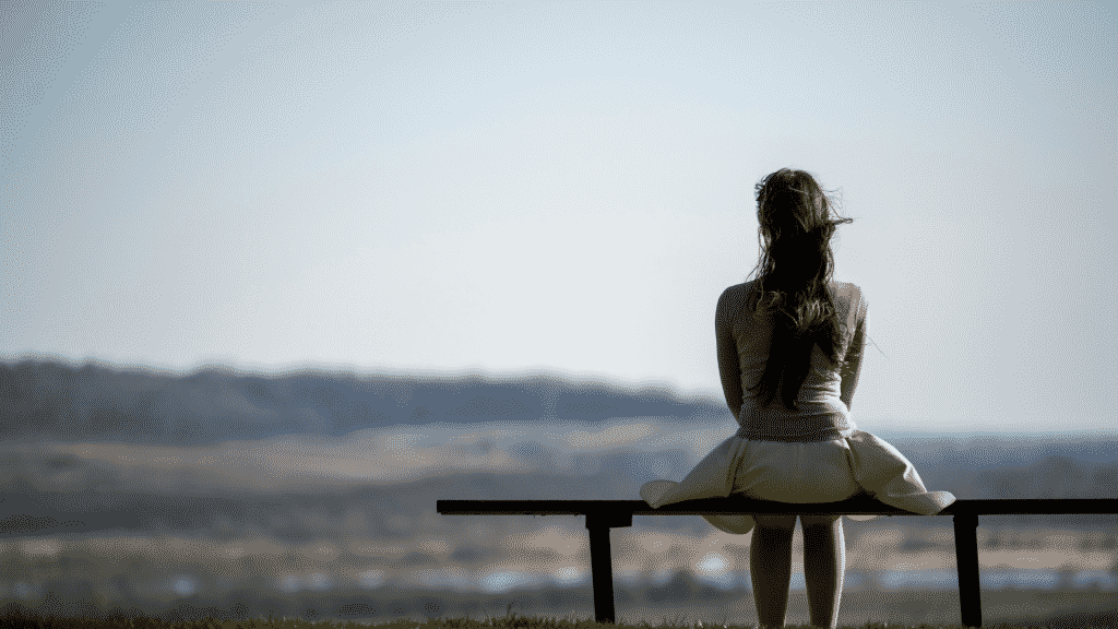 Mulher sentada sozinha em um banco contemplando o horizonte