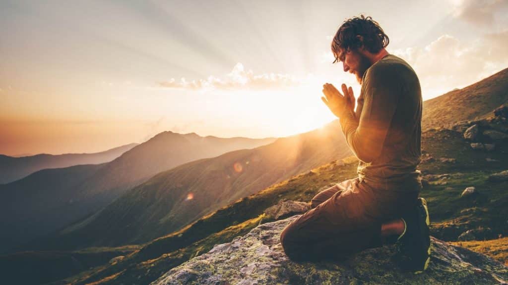 Um homem orando no pico de uma montanha.