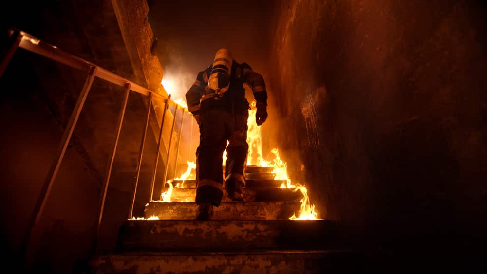 Um bombeiro subindo escadas de um prédio em chamas.