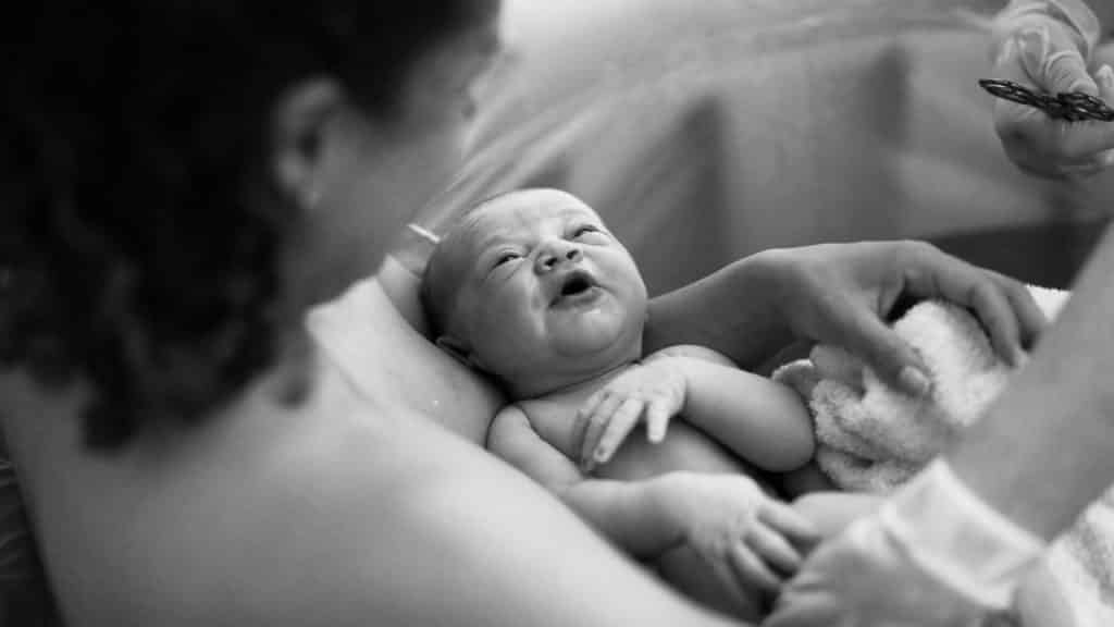 Uma mulher segurando em seu colo um bebê recém-nascido. 