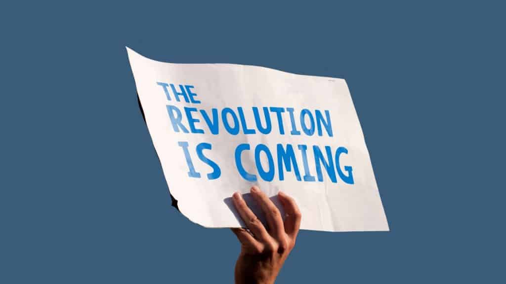Uma mão segurando uma placa cujo texto escrito é "the revolution is coming".