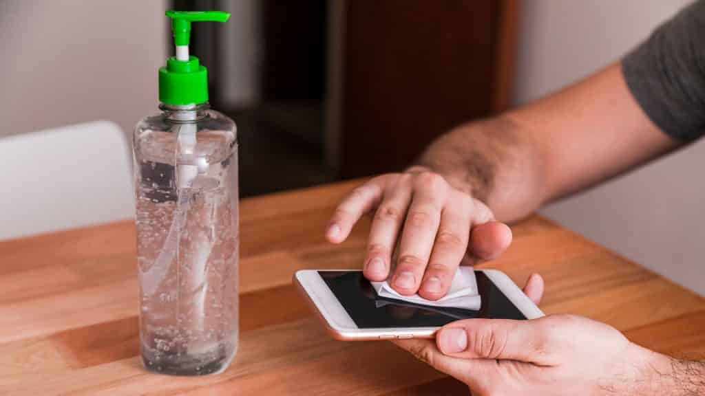 Um homem limpando um celular com álcool em gel.