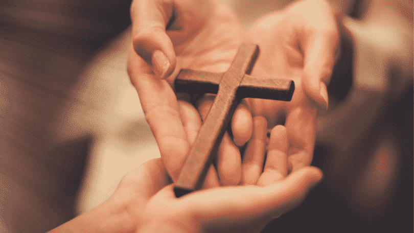 Duas mãos humanas segurando uma miniatura de madeira de uma cruz.