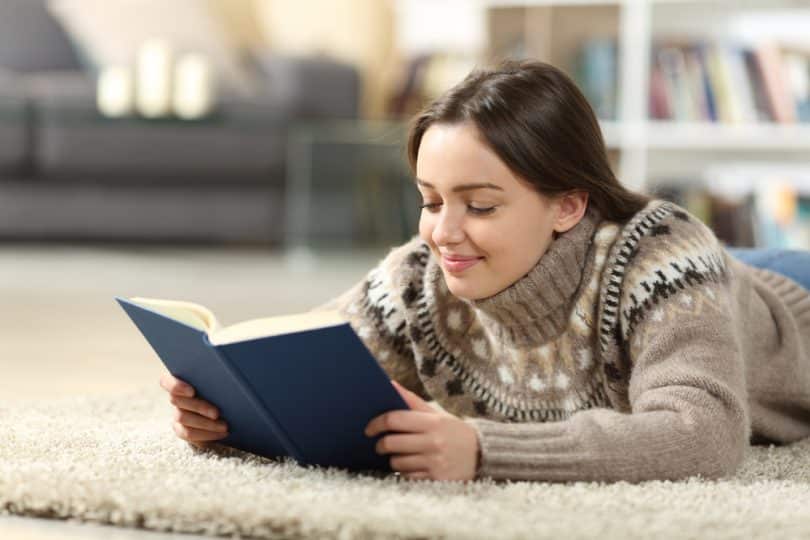 Uma garota, deitada num tapete, a ler um livro.