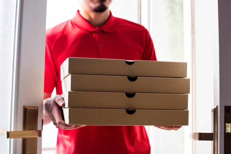 Um entregador de pizzas segurando várias caixas de pizza.