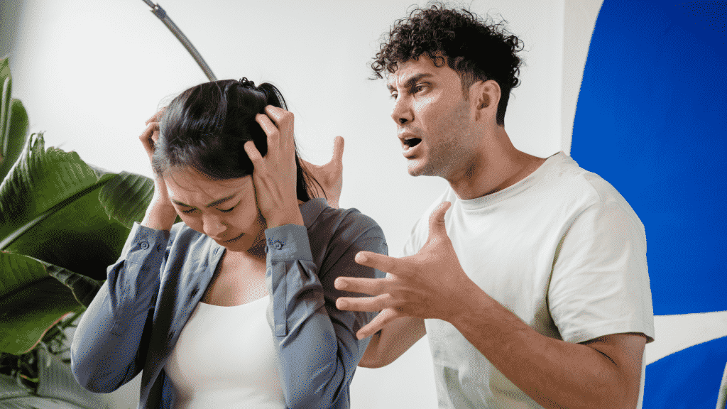 Uma mulher asiática tapando seus ouvidos e, à direita dela, um homem branco gritando.