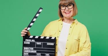 Uma mulher sorrindo e segurando um claquete de cinema.