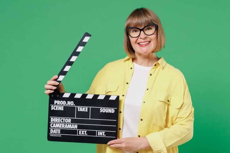 Uma mulher sorrindo e segurando um claquete de cinema.