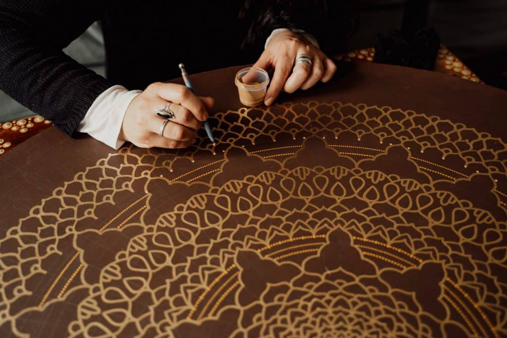 Mulher desenhando uma mandala em uma mesa redonda.