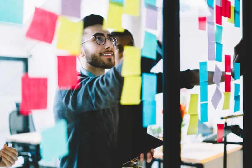 Homem usando óculos olhando para cima para uma parede repleta de post-its