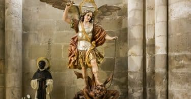 Escultura de São Miguel Arcanjo com sua espada em mãos pisando em cima de um demônio