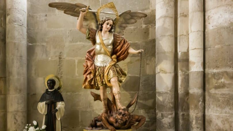 Escultura de São Miguel Arcanjo com sua espada em mãos pisando em cima de um demônio