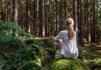 Mulher em uma floresta, sentada de costa para a câmera, ouvindo o silêncio da natureza.
