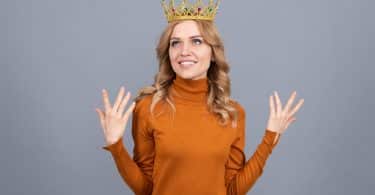 Mulher usando uma coroa gesticulando com as mãos para cima representando o narcisismo
