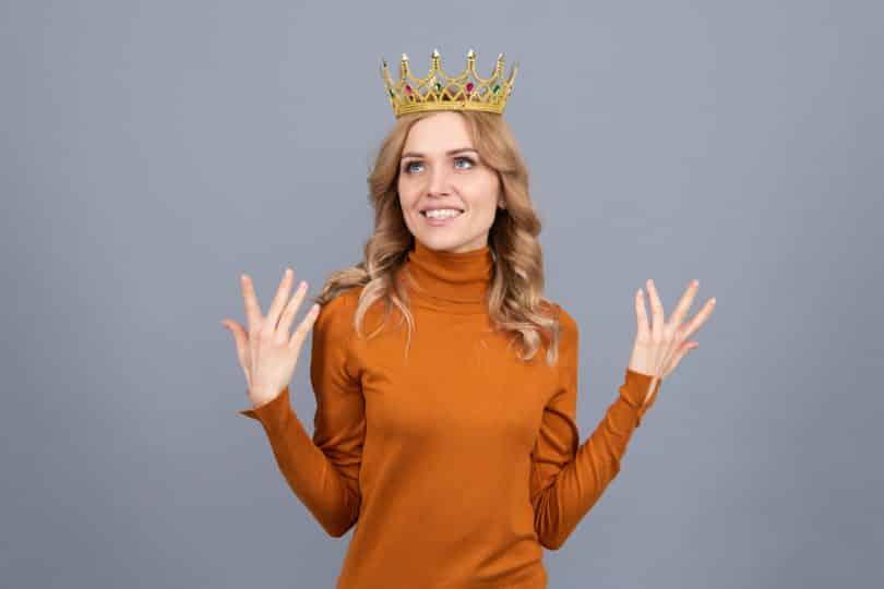 Mulher usando uma coroa gesticulando com as mãos para cima representando o narcisismo