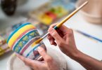 Mãos femininas pintando um vaso de argila.