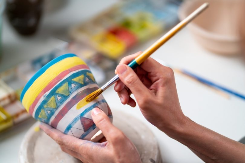 Mãos femininas pintando um vaso de argila.