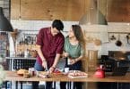 Casal cozinhando em uma bancada de madeira dando risada