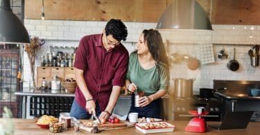 Casal cozinhando em uma bancada de madeira dando risada