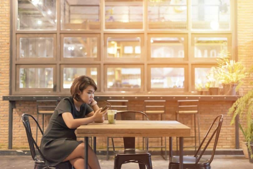 Mulher sentada sozinha em uma mesa de bar usando o celular