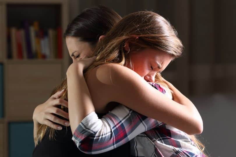 Duas mulheres abraçadas, ambas de olhos fechados e chorando enquanto se reconciliam