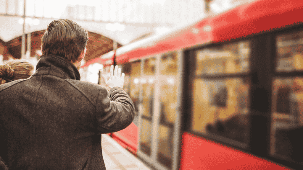 Homem acenando para um trem que está partindo de estação representando deixar as coisas para trás