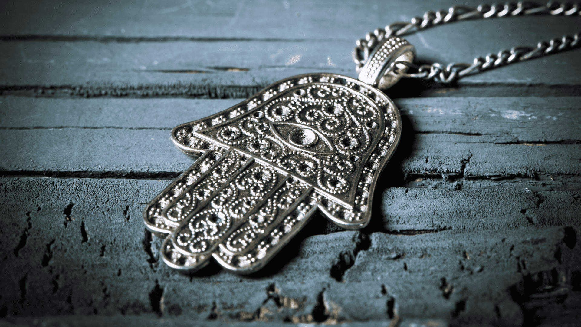 Imagem de um colar de prata com o símbolo Hamsá apoiado numa superfície de madeira