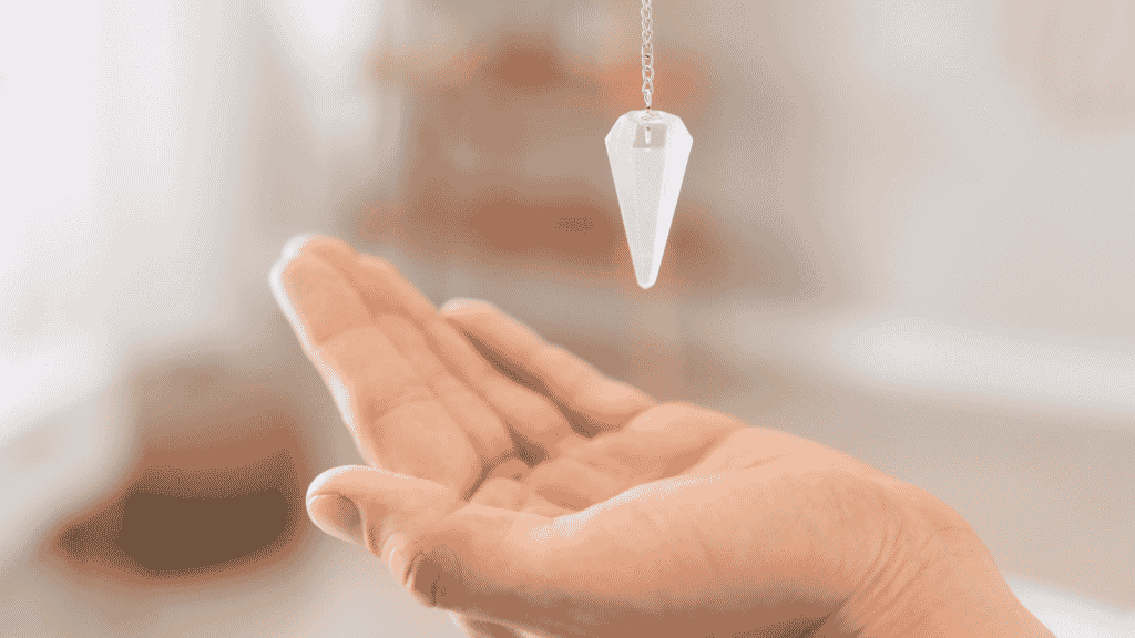 Mão de uma pessoa embaixo de um pêndulo de cristal pendurado