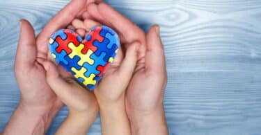 Mãos infantis e adultas segurando um coração colorido de quebra-cabeça