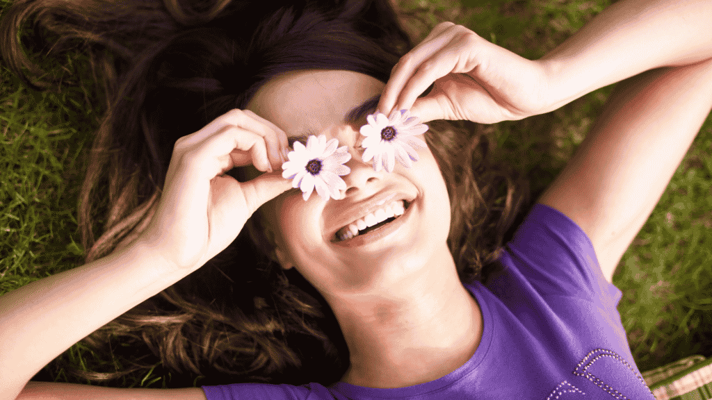 Mulher deitada na grama sorrindo cobrindo seus olhos com flores