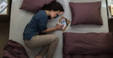 Uma mulher chorando na cama. Ela segura um quadro.