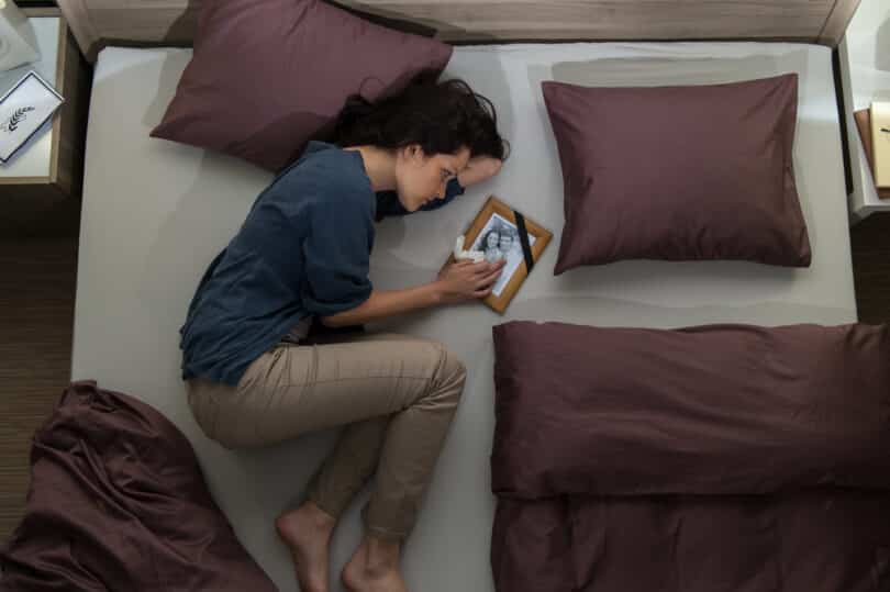Uma mulher chorando na cama. Ela segura um quadro.