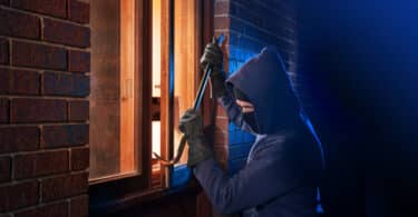 Um ladrão arrombando uma janela de uma casa.