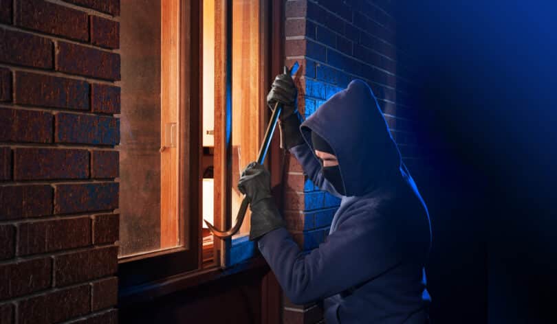 Um ladrão arrombando uma janela de uma casa.