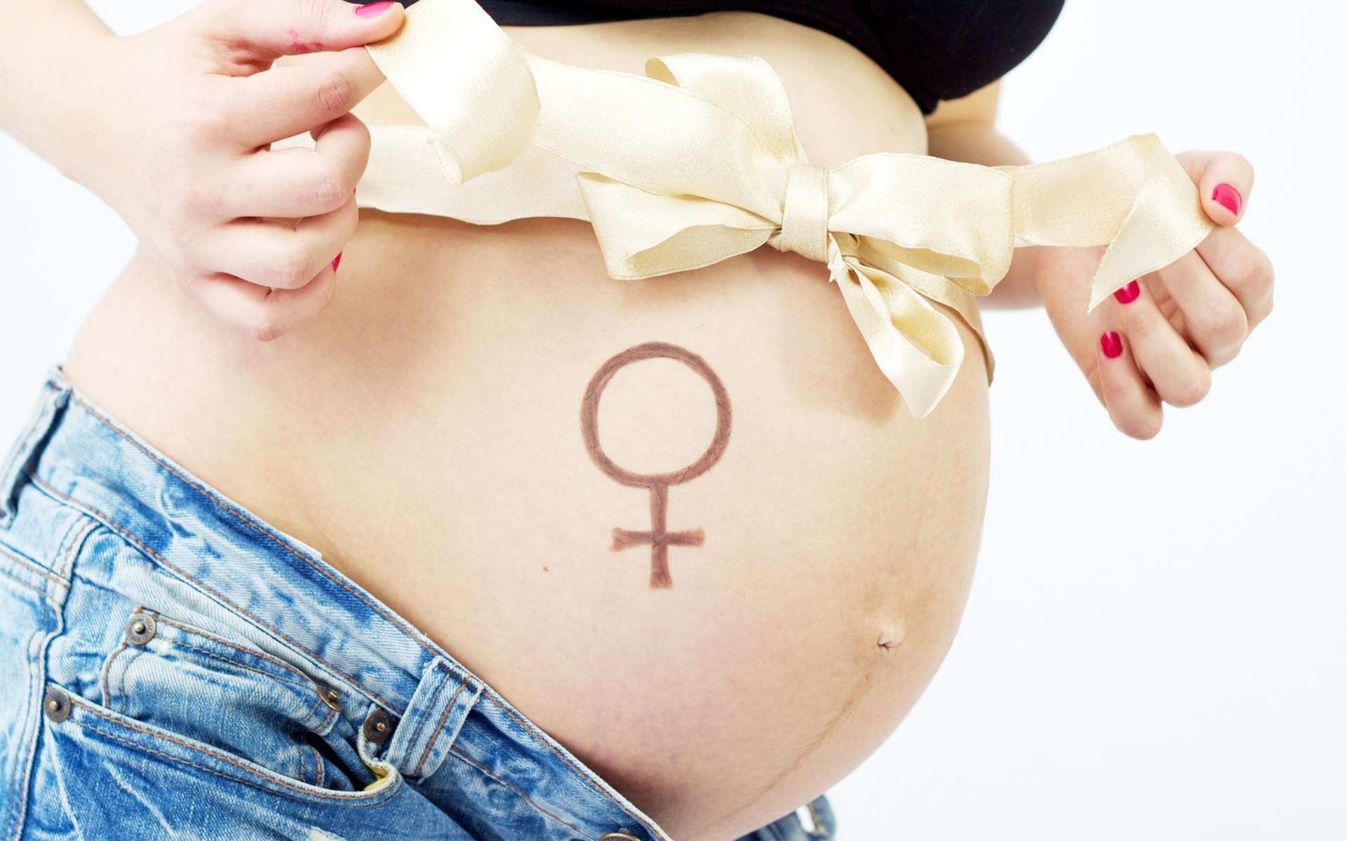 Uma mulher grávida enfitando sua própria barriga. Abaixo dessa fita, um símbolo que comumente representa o sexo feminino.