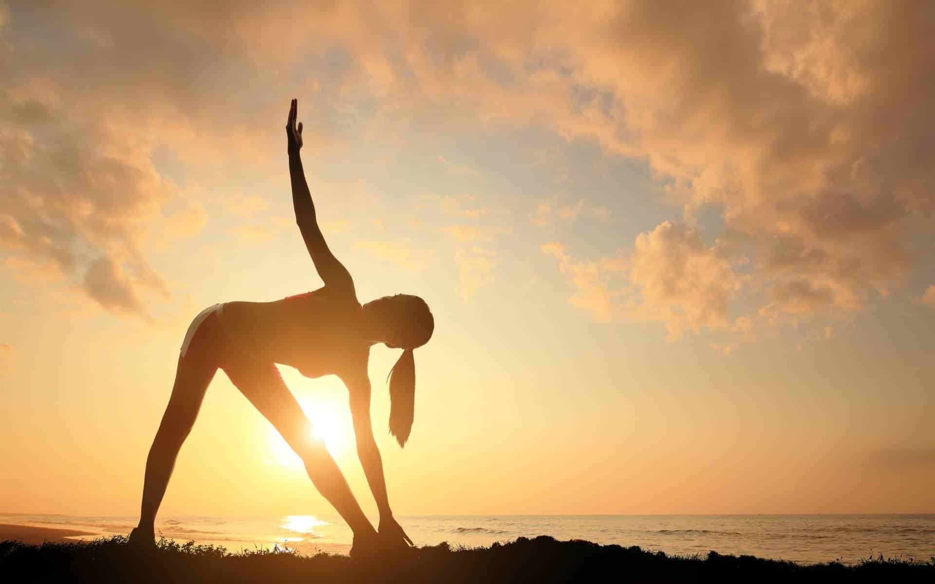 Uma mulher realizando uma posição do yoga durante o nascer do sol.