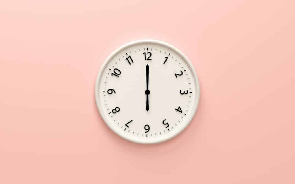Um relógio de parede numa parede rosa.