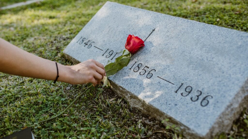 Uma pessoa colocando uma rosa no túmulo de um morto.