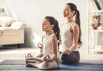 Uma pequena garota e uma mulher meditando numa sala.