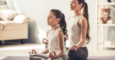 Uma pequena garota e uma mulher meditando numa sala.