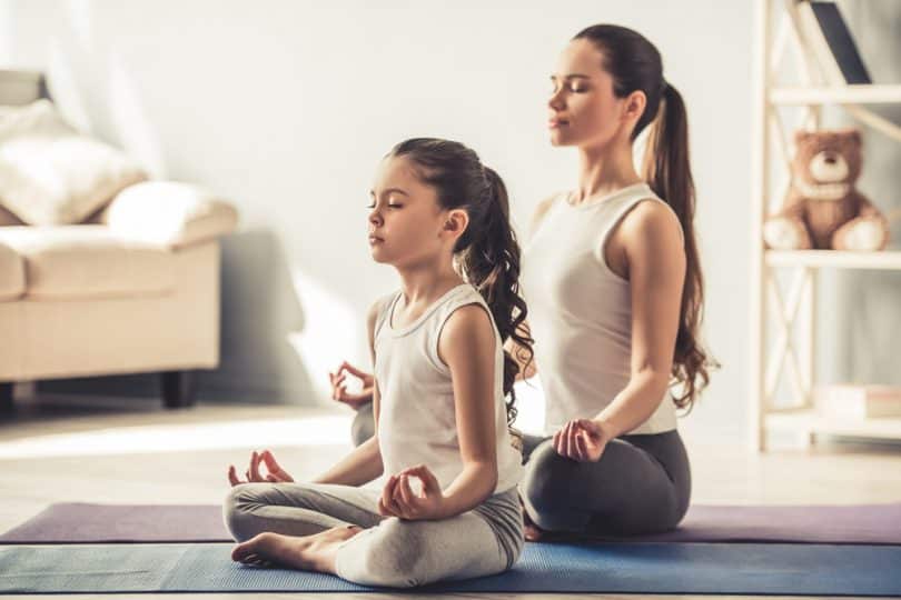 Uma pequena garota e uma mulher meditando numa sala.