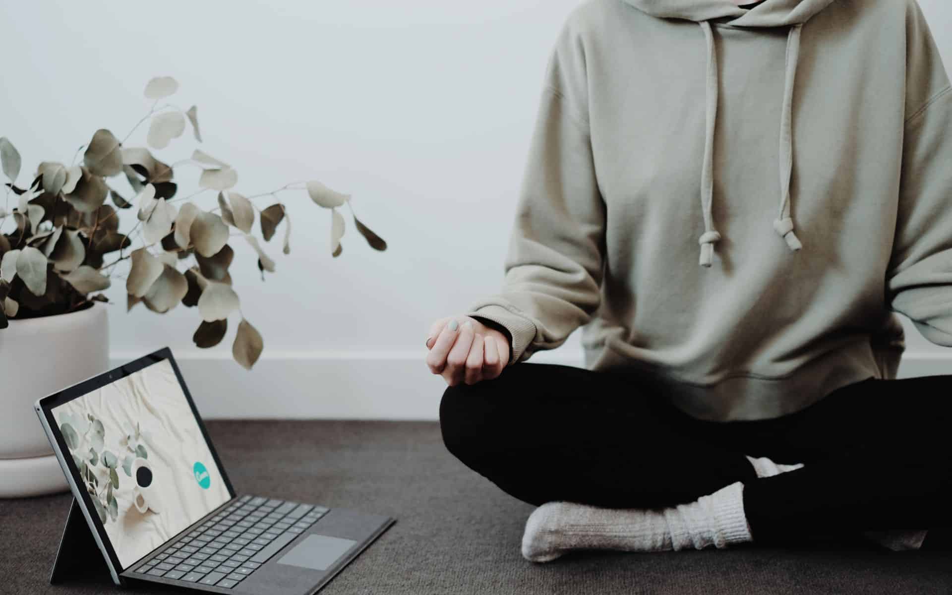 Uma pessoa meditando próxima a um notebook.