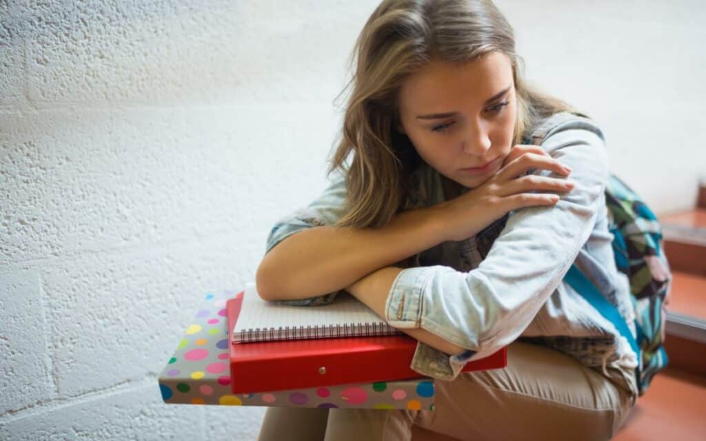 Uma garota debruçando a sua cabeça em alguns de seus materiais escolares.