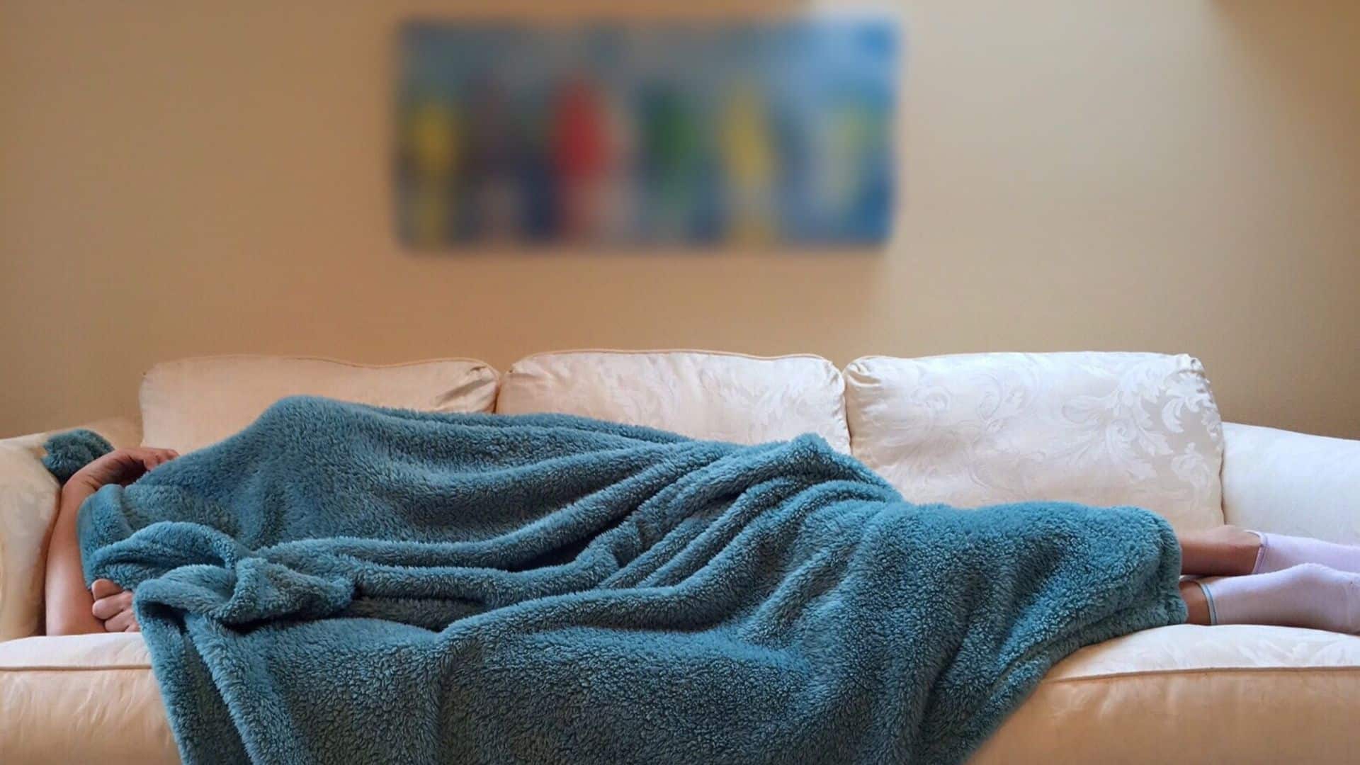 Uma pessoa dormindo completamente coberta num sofá.