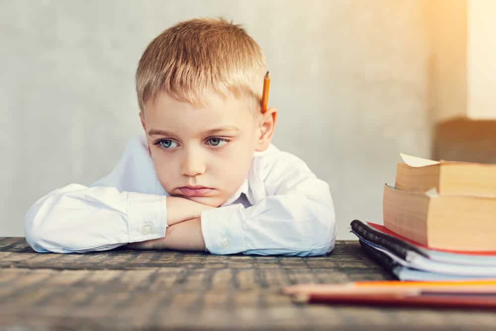 Uma criança triste debruçando sua cabeça sobre uma mesa.