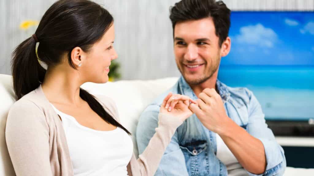 Um homem e uma mulher entrelaçando seus dedos mindinhos.