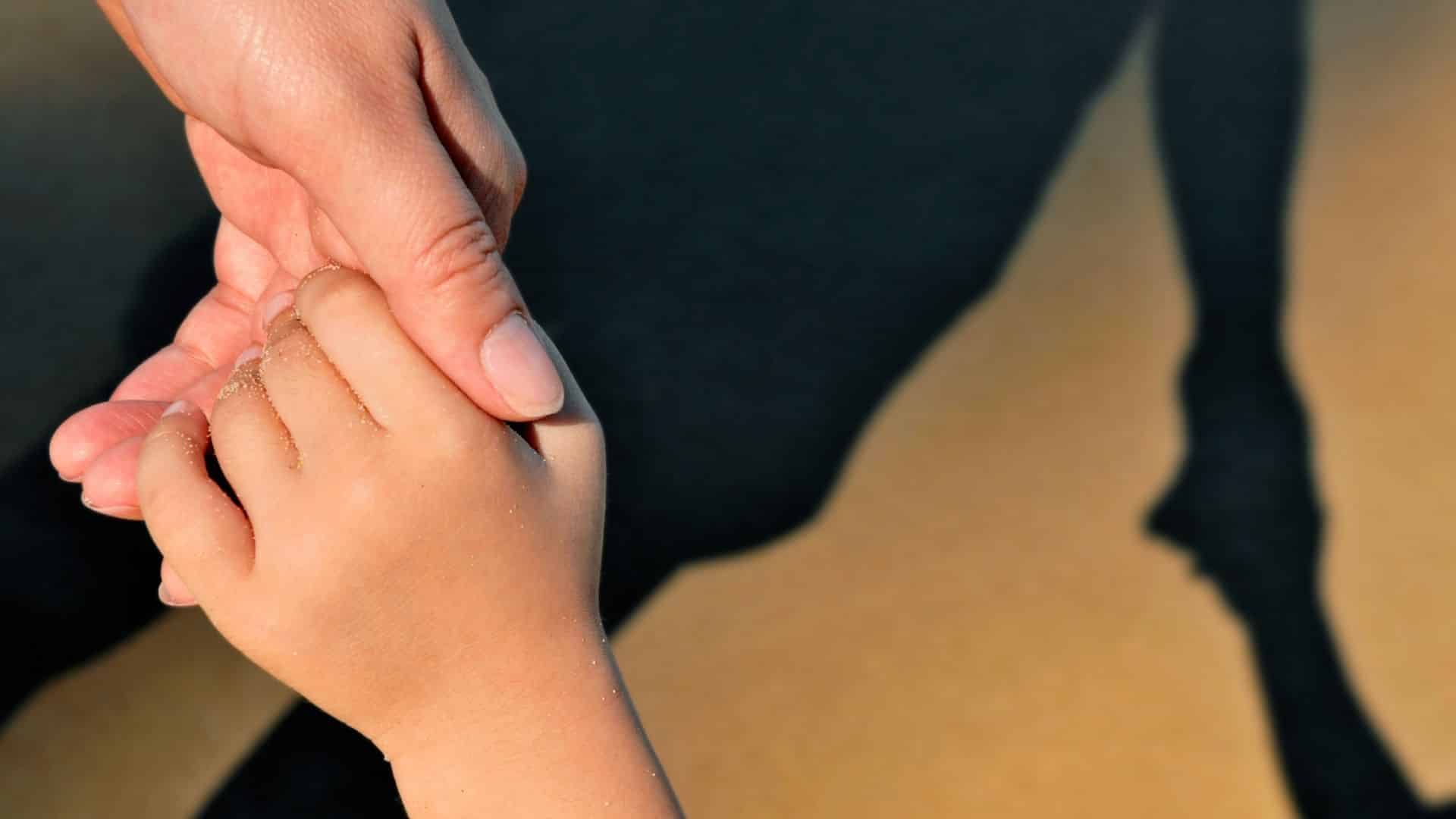 Uma mão adulta feminina segurando uma mão de uma criança.